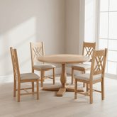 A 5-piece dining set featuring a Chatsworth round wooden table and four matching chairs with light beige upholstered seats, shown in a bright, modern room with natural light.