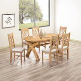 A 7-piece round wooden dining table set with six matching chairs featuring light beige upholstered seats, shown in a bright dining room with wood-look flooring and a large window.