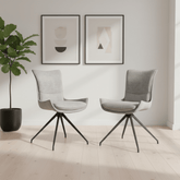 Two modern light gray upholstered swivel dining chairs with black metal tripod bases, shown in a bright minimalist room with a potted plant and framed wall art.