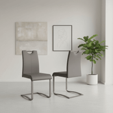 Two modern gray upholstered dining chairs with curved metal cantilever legs, shown in a minimalist room setting with framed wall art and a potted plant.
