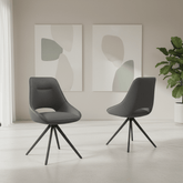 Two modern dark gray swivel dining chairs with black metal tripod legs, shown in a minimalist room setting with abstract wall art and a potted plant.