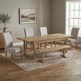 A light oak wood dining table set in a dining room with four light beige upholstered chairs, a matching wooden bench, and a patterned area rug.