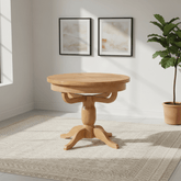 Chatsworth Oak Round Extending Dining Table with a natural oak finish, set on a cream patterned area rug in a bright room with two framed abstract prints and a potted fiddle-leaf fig plant.