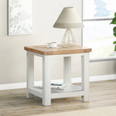A lifestyle image of a Foxington Lamp Table with an off-white painted frame, lower shelf and a light natural wood top.
