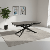 Modern dining table with X-shaped legs in a minimalistic room with a plant and abstract art.