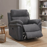 A dark gray recliner chair with white contrast stitching, shown in a fully furnished living room with a wooden floor, bookshelf, and window.
