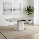 Dining table with marble-like surface and white base in a room with a plant and wall art.