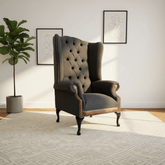 Gray wingback chair in a room with a plant and framed art on the wall.