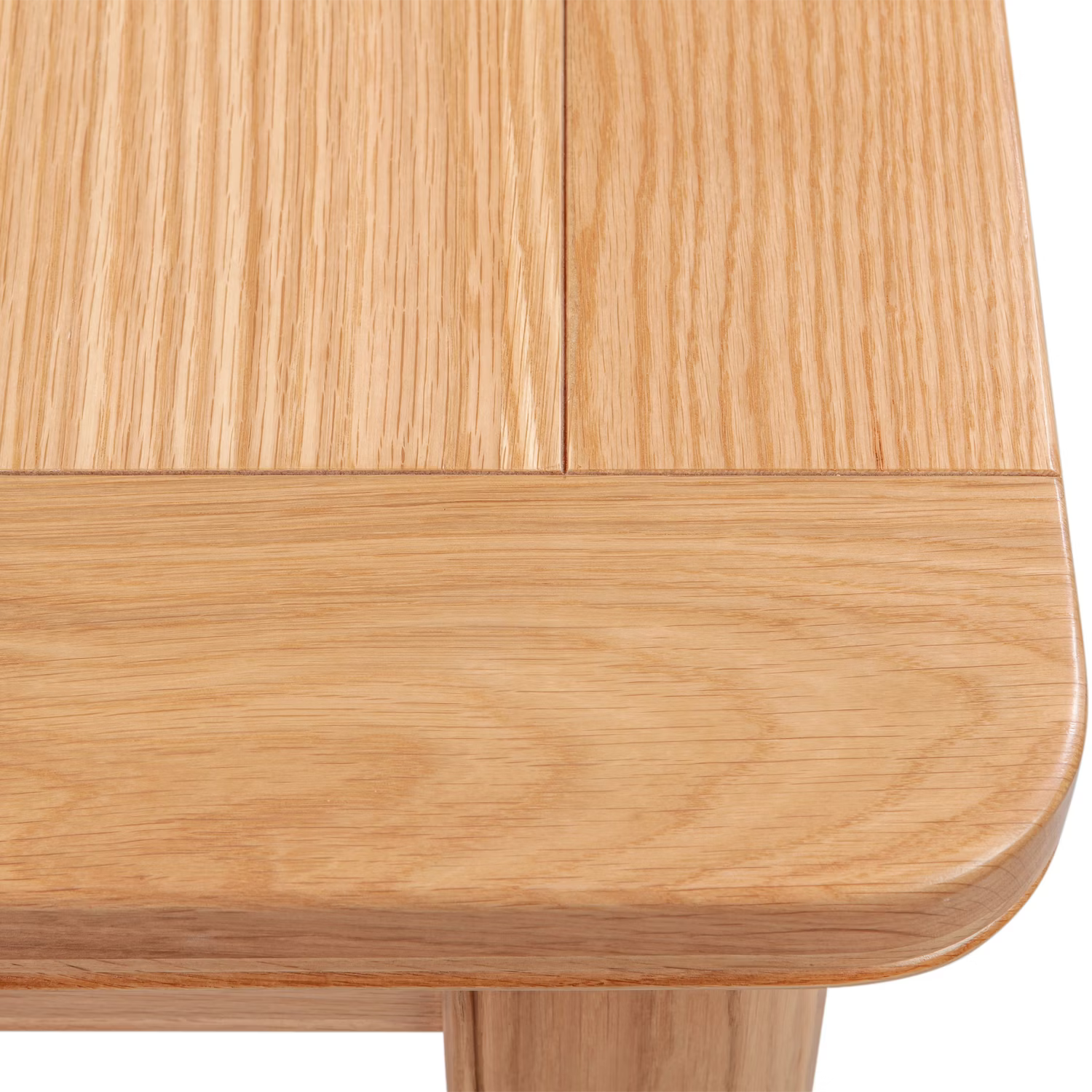 Close-up detail of a Chatsworth Oak Extending Dining Table corner, showing the rounded edge, tabletop grain, and part of the leg on a white background.