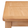 Close-up of a light oak wood table showing the top surface with a raised panel design and rounded corner.