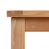 Close-up of a light oak wood table corner showing the mitered top joint, leg, and front apron on a white background.