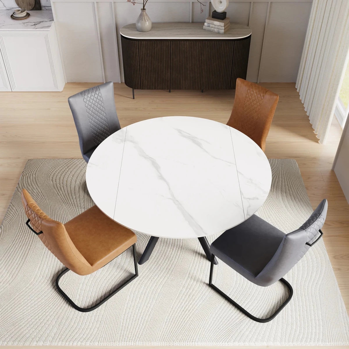 A round white marble-patterned dining table surrounded by four modern upholstered chairs in brown, gray, and black, set on a textured cream rug in a bright, contemporary dining room.