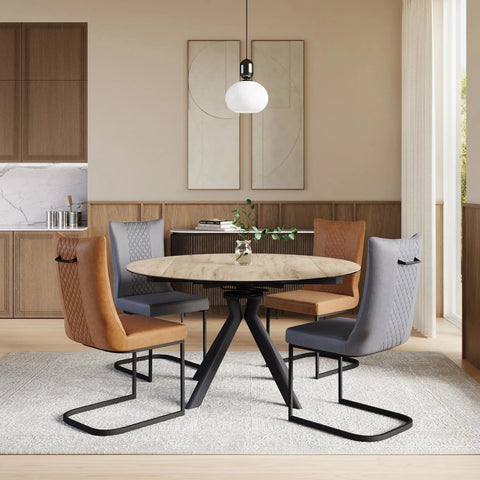 A modern dining set featuring a round light-wood table with a black metal pedestal base, surrounded by four upholstered chairs in gray and tan leather, set on a light gray rug in a contemporary dining room.