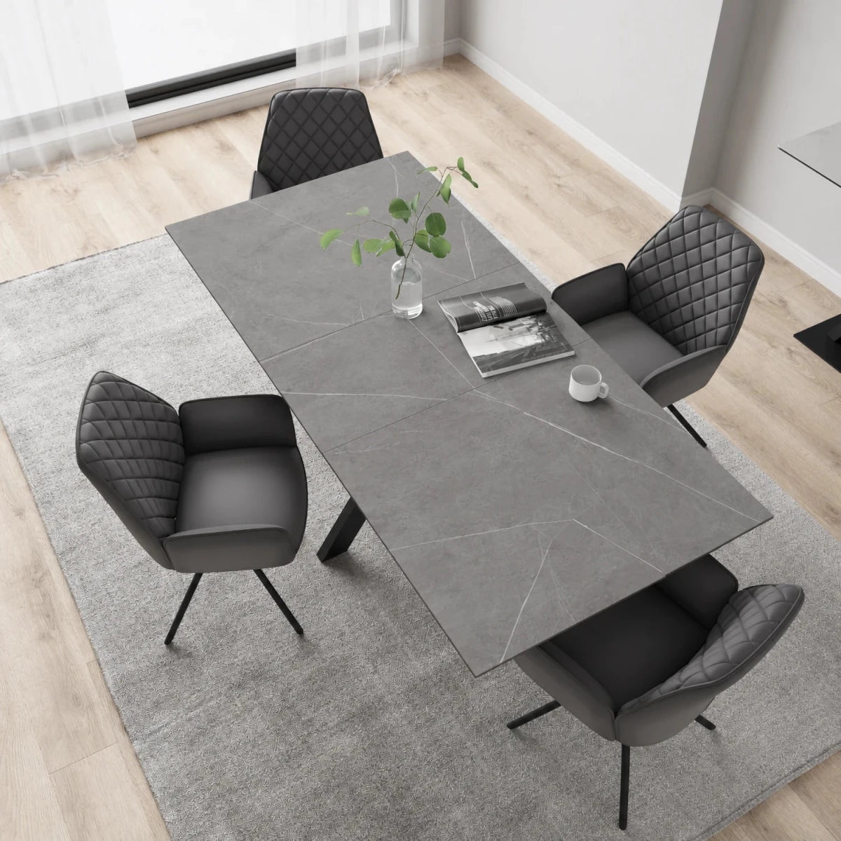 A modern dining room with a rectangular Amari Matt Grey Ceramic Dining Table & Lina Chairs on a light gray rug, with a small plant and cup on the table.