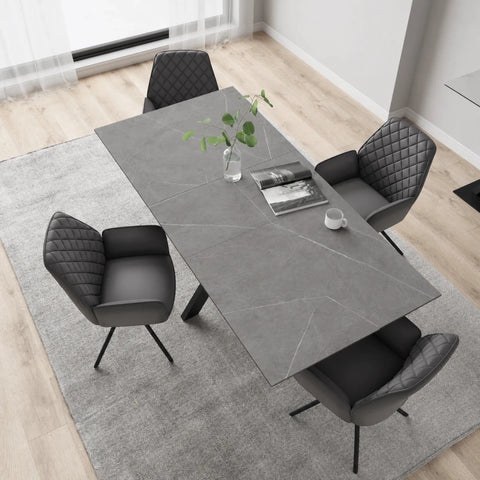 A modern dining room with a rectangular Amari Matt Grey Ceramic Dining Table & Lina Chairs on a light gray rug, with a small plant and cup on the table.