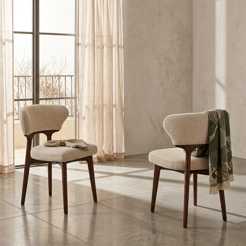 Two chairs with wooden frames and beige cushions in a room with large windows and curtains.
