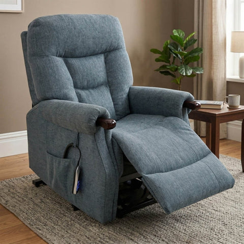 A blue-gray upholstered recliner chair with the seat extended, shown in a living room setting with a side table, plant, and window in the background.