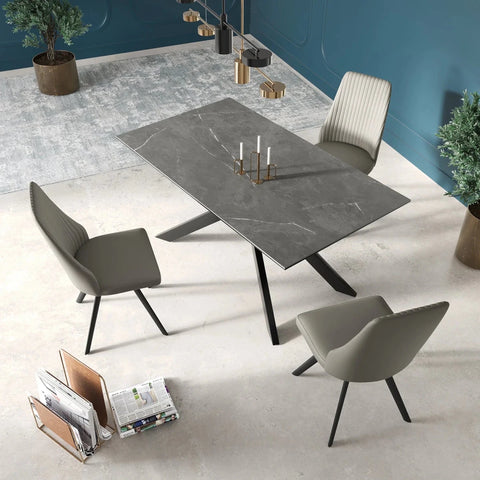A modern dining set featuring a rectangular dark gray marble-look sintered stone ceramic  table with black legs, surrounded by four gray upholstered chairs with black tapered legs, set in a contemporary room with a blue wall and light concrete floor.