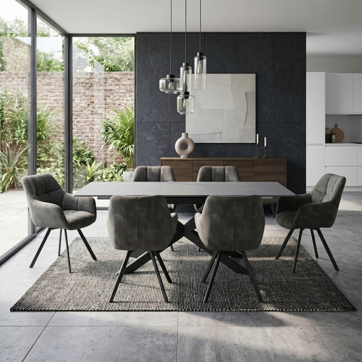 A modern dining room set featuring a rectangular gray stone table surrounded by six gray velvet upholstered chairs with black metal legs, set on a textured gray rug in a contemporary dining space.