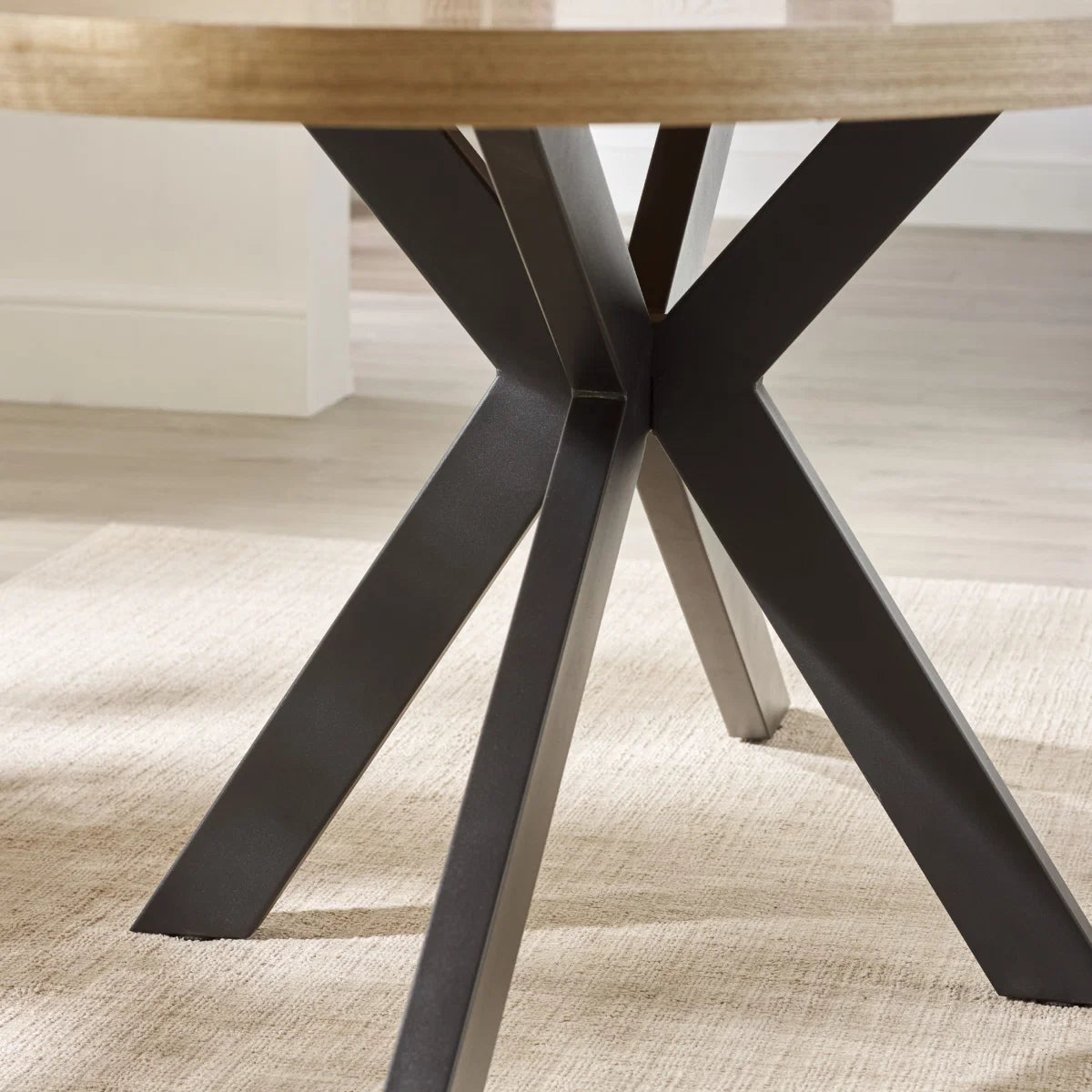 Close-up of a wooden table with a black metal base on a textured floor.
