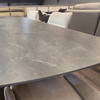 A modern rectangular dining table with a gray stone-look surface and white chairs in a furniture showroom.