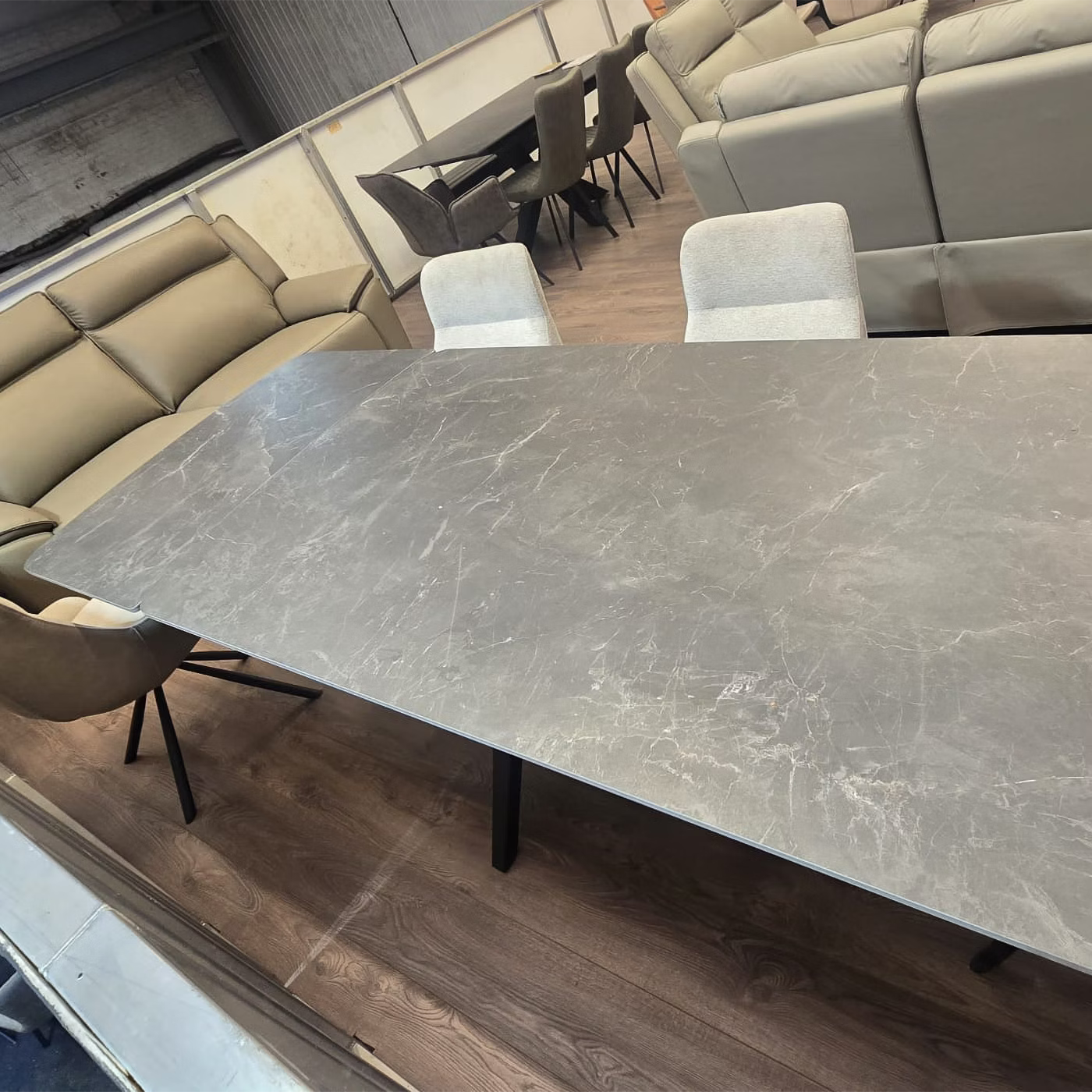 Beatrix Slate Mist Sintered Stone Extending Dining Table with a gray slate  marble-patterned Sintered stone top and black metal legs, surrounded by  upholstered chairs in a furniture showroom.