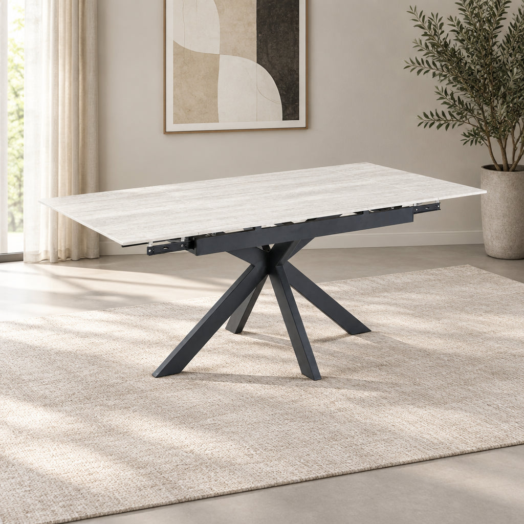 A rectangular dining table with a ivory sintered stone ceramic top and a dark charcoal gray geometric cross-style pedestal base, shown on a solid white background.