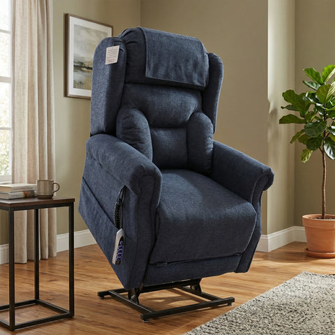 A dark blue upholstered power lift recliner chair shown in a staged living room setting with wood floors, a side table, framed wall art, and a potted plant.