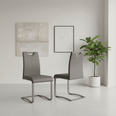 Two modern gray upholstered dining chairs with curved metal cantilever legs, shown in a minimalist room setting with framed wall art and a potted plant.