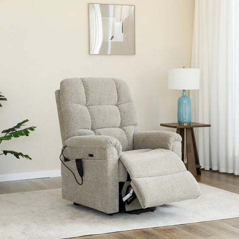 A light beige upholstered recliner chair with a footrest extended, shown in a styled living room setting with a side table, lamp, curtains, and wall art.