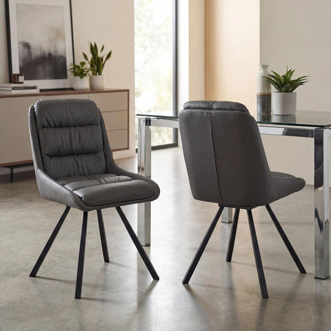 Two modern gray upholstered dining chairs with black metal legs, shown in a bright contemporary dining room next to a glass-top table.