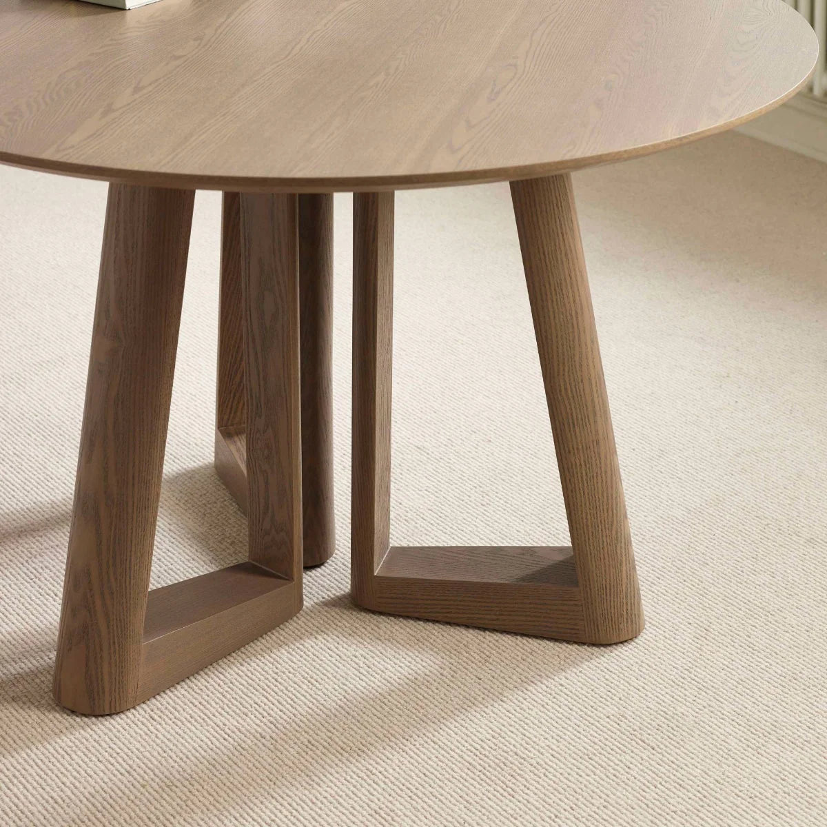 Close up of Cara 120cm Smokey Oak Effect Round Dining Table. Featuring a warm wood-effect finish, sculptural architectural base and elegant circular top.