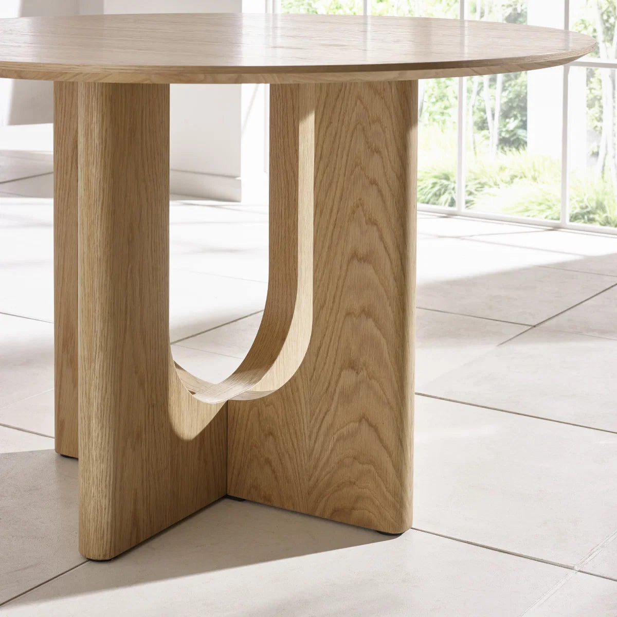 Cove 120cm Natural Oak Effect Round Dining Table, with a sculptural intersecting pedestal base and beautiful natural wood grain finish.