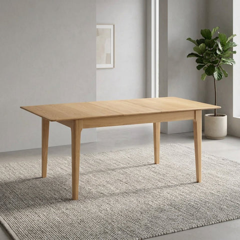 A light natural wood extendable dining table with four tapered legs, shown from a three-quarter angle on a solid white background.