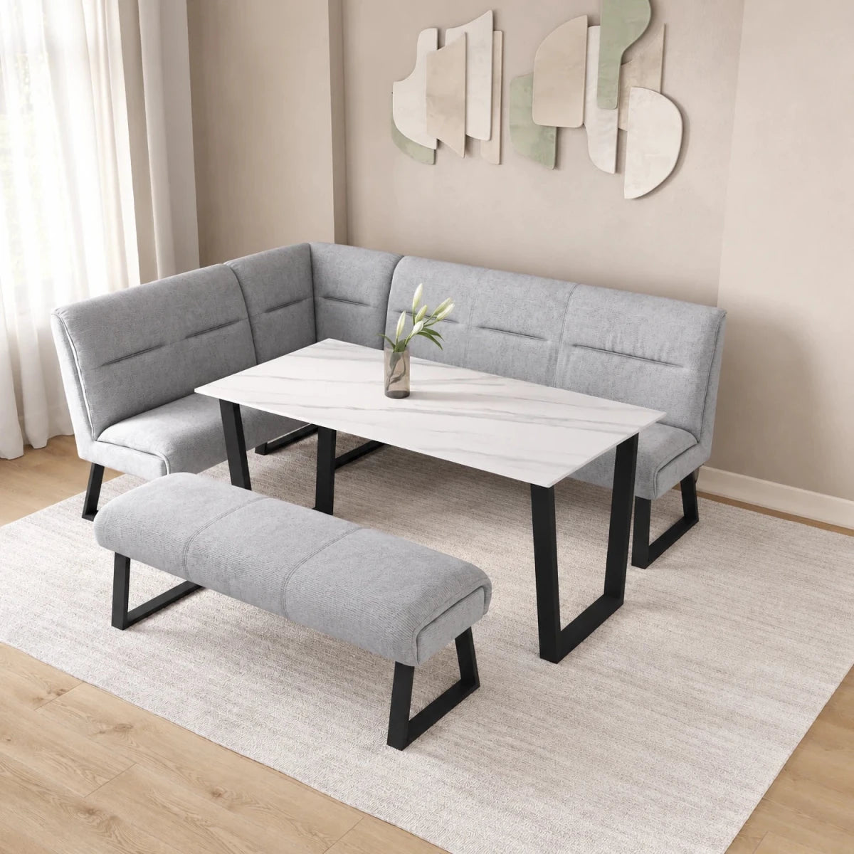 A modern L-shaped corner banquette seating set with a matching bench, featuring light gray upholstered cushions and black metal legs, arranged around a white marble-patterned rectangular table in a styled dining room setting.