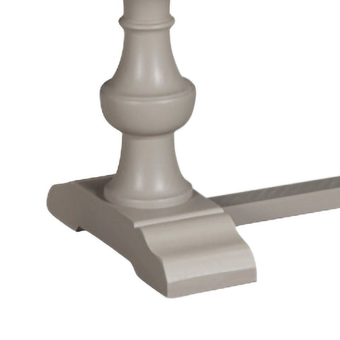 Close-up of a decorative column base of A rustic dining bench with a light natural wood seat and a painted gray base and stretcher bar, shown on a plain white background.