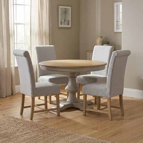 Chateau A round pedestal dining table with a light natural wood top and a distressed grey painted base with Grey Fabric Upholstered Chairs