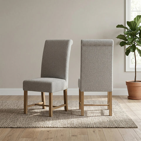 Two upholstered dining chairs with light gray fabric and natural wood legs, shown from the front and back on a woven rug in a bright room with a potted plant.
