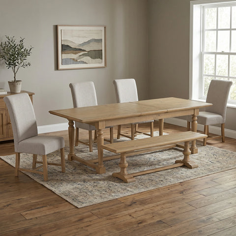 A light oak wood dining table set in a dining room with four light beige upholstered chairs, a matching wooden bench, and a patterned area rug.