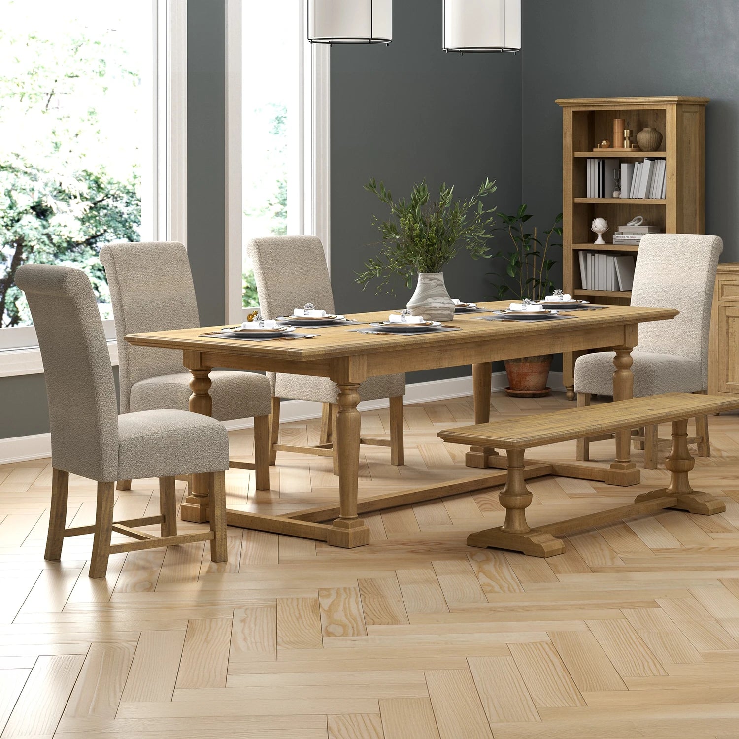 A light oak wood dining table set with six upholstered dining chairs, a wooden bench, and tableware, staged in a modern dining room with gray walls and a wood herringbone floor.