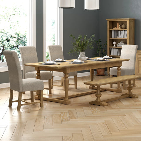 A light oak wood dining table set with six upholstered dining chairs, a wooden bench, and tableware, staged in a modern dining room with gray walls and a wood herringbone floor.