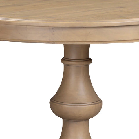 Close-up of a round wooden table with a turned pedestal leg in a light natural wood finish, shown against a plain white background.