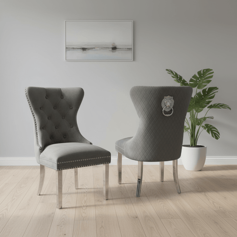 Two dark grey Velvet Fabric upholstered dining chairs with silver metal legs and nailhead trim, Lion Knocker back shown in a styled room with a potted plant and wall art.