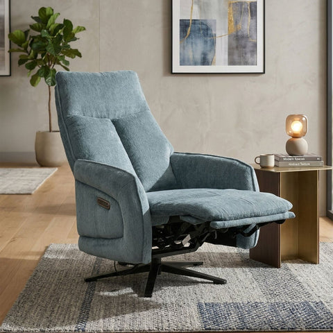 A light blue textured fabric recliner chair with a black swivel base, styled in a modern living room setting next to a wooden side table with a lit lamp.