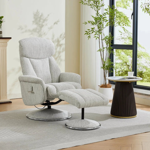 A light gray upholstered recliner chair with matching ottoman in a bright, modern living room setting with a window, potted plant, and side table.