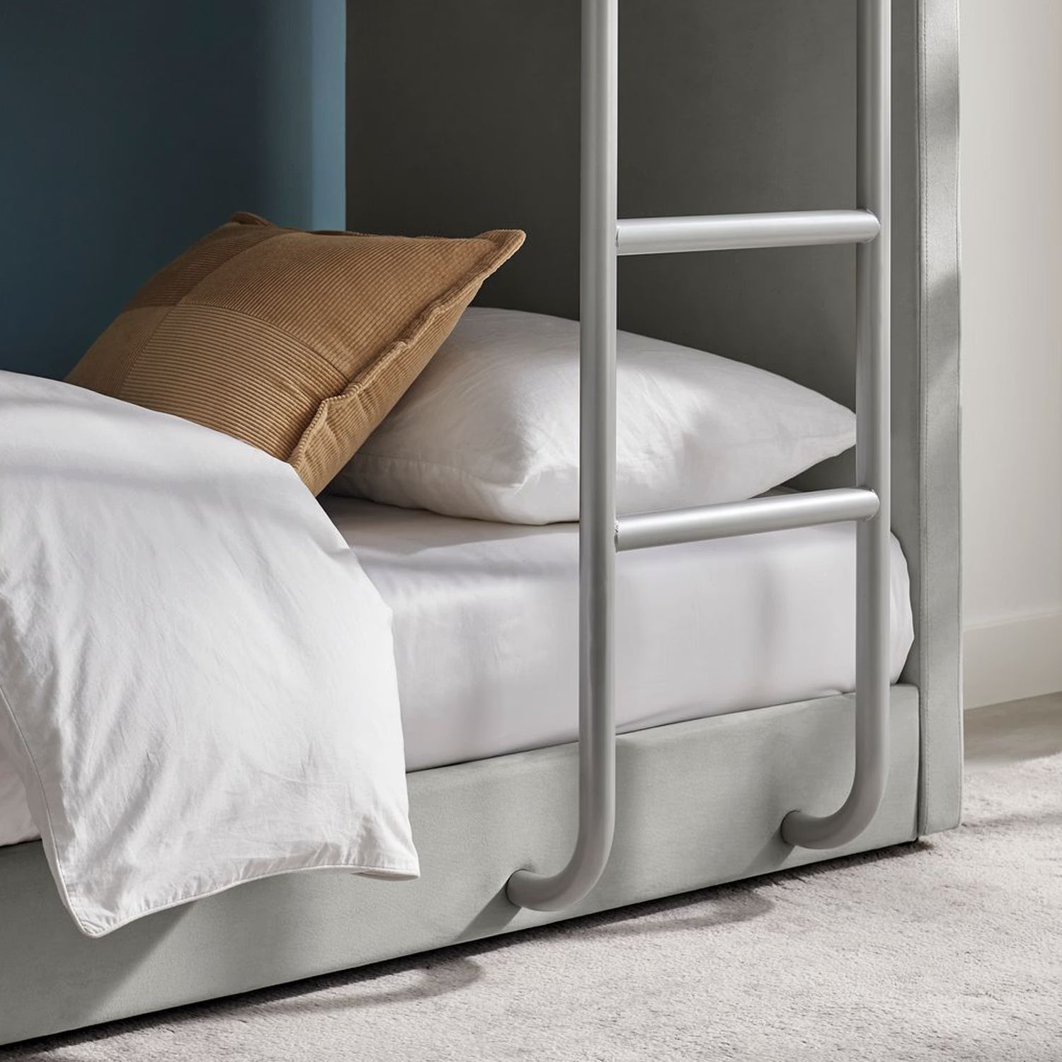 A close-up of a bed frame with a ladder on the side in a light grey upholstered finish.