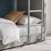 A close-up of a bed frame with a ladder on the side in a light grey upholstered finish.