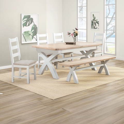 Lifestyle image of a Foxington Painted Dining Set, including a rectangular table, two chairs, and a bench, shown in a bright, modern dining room setting with a beige rug and wood flooring.