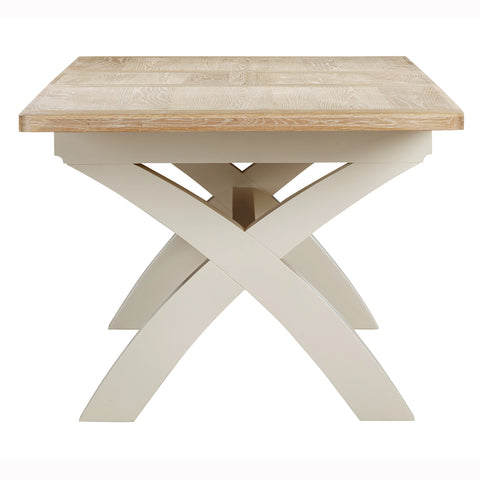A close up of the Foxington dining table uwood top and a cream-colored X-shaped pedestal base, shown against a plain white background. 