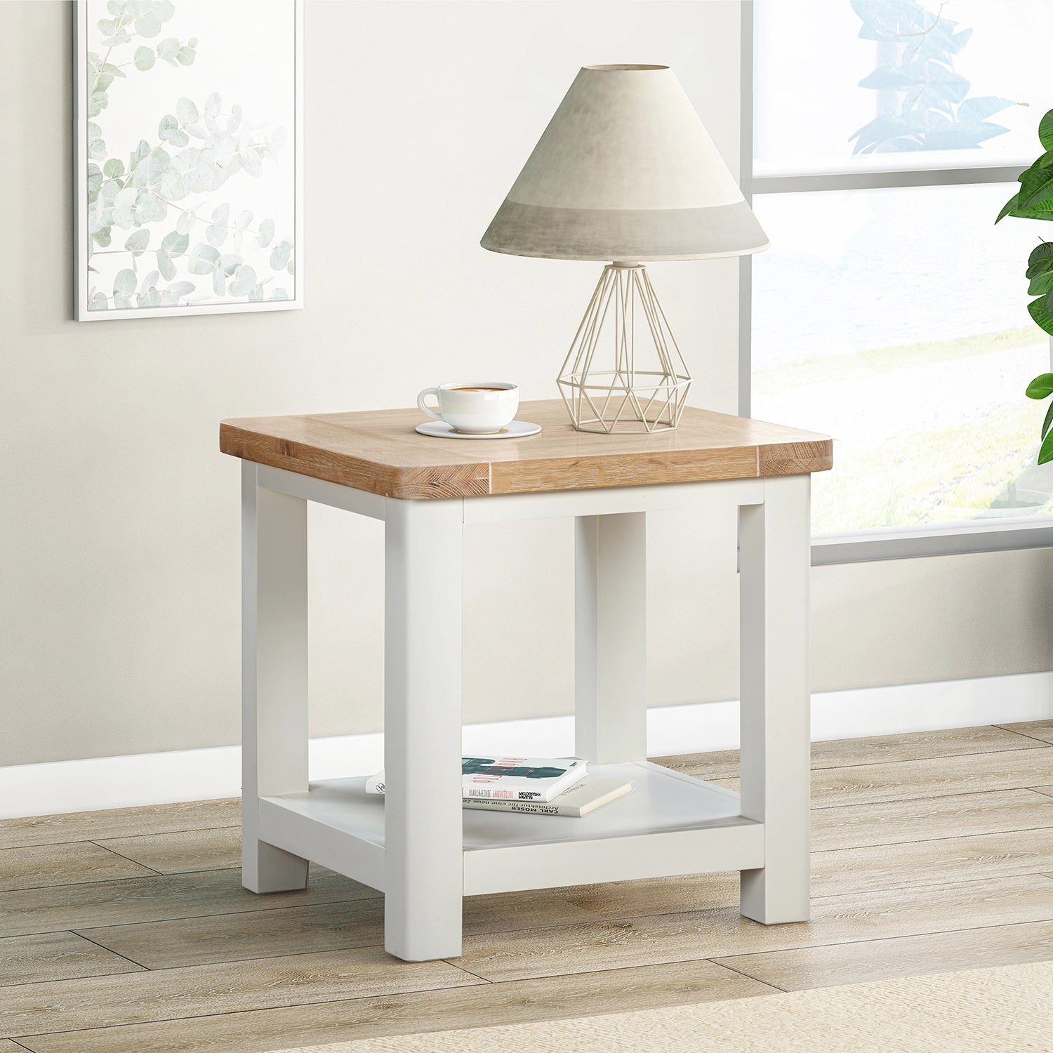 A lifestyle image of a Foxington Lamp Table with an off-white painted frame, lower shelf and a light natural wood top.